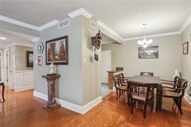 dining area with a chandelier, visible vents, ornamental molding, and wood finished floors