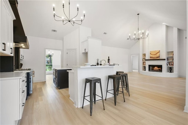 kitchen with light wood-style floors, stainless steel range with gas stovetop, high vaulted ceiling, a chandelier, and a kitchen island