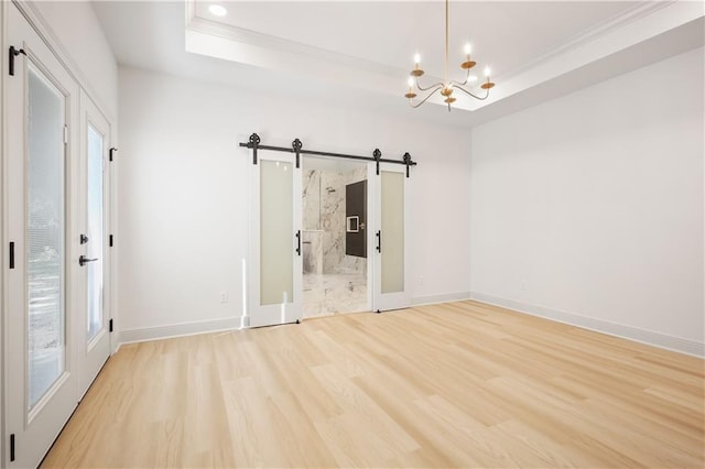 spare room with crown molding, an inviting chandelier, a barn door, a tray ceiling, and light wood finished floors