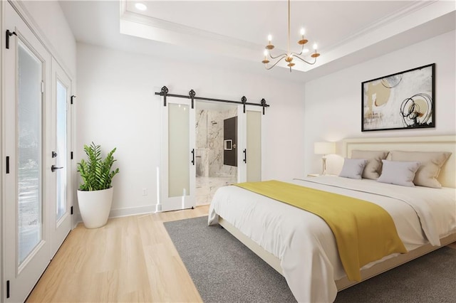 bedroom featuring a barn door, light wood finished floors, an inviting chandelier, ornamental molding, and a tray ceiling