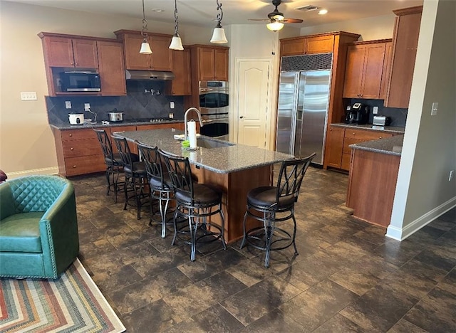 kitchen featuring under cabinet range hood, stainless steel appliances, baseboards, and a sink
