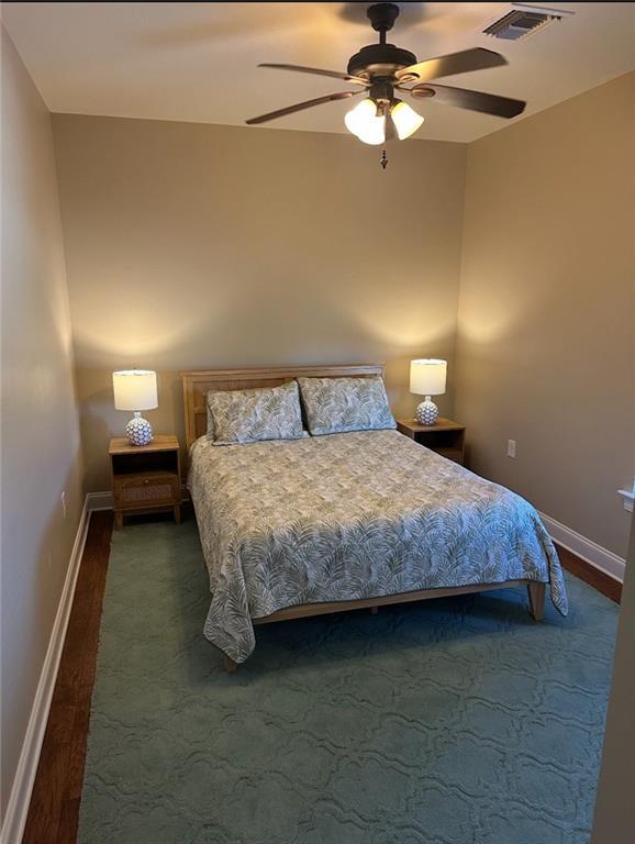 bedroom featuring visible vents, baseboards, ceiling fan, and wood finished floors
