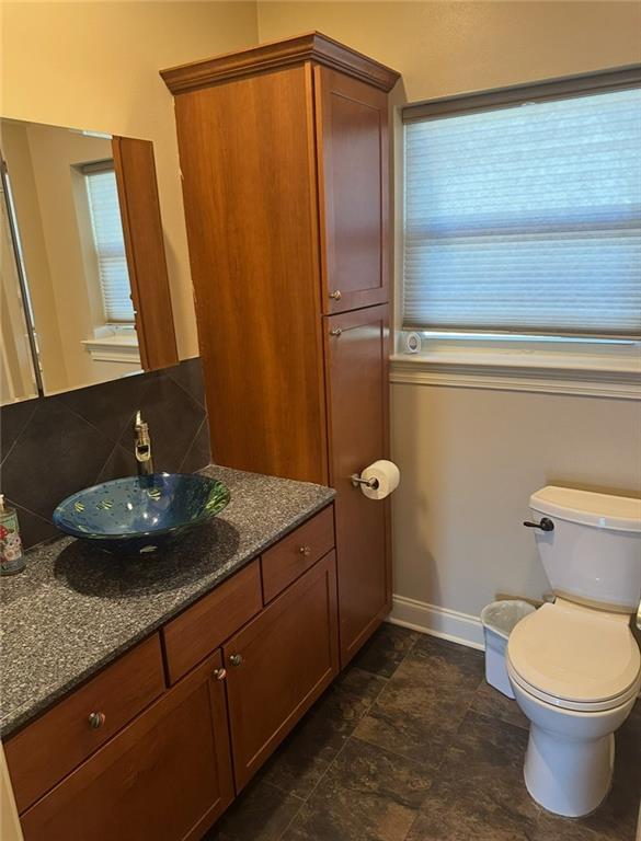 half bathroom featuring baseboards, vanity, toilet, and a wealth of natural light