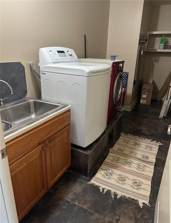 clothes washing area featuring a sink, cabinet space, washing machine and dryer, and stone finish flooring