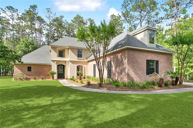 view of front of home with roof with shingles, brick siding, and a front yard