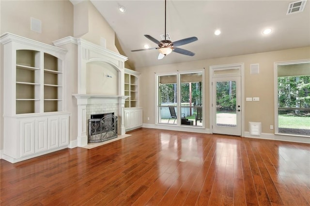 unfurnished living room with a brick fireplace, a ceiling fan, visible vents, and wood finished floors