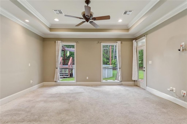 empty room with light colored carpet, a tray ceiling, visible vents, and ornamental molding