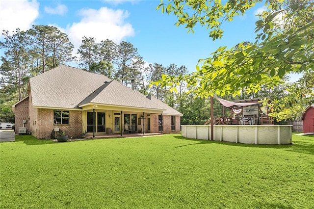 rear view of property featuring a lawn, roof with shingles, brick siding, and an outdoor pool