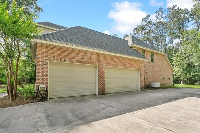 view of side of home featuring roof with shingles, an attached garage, concrete driveway, and brick siding