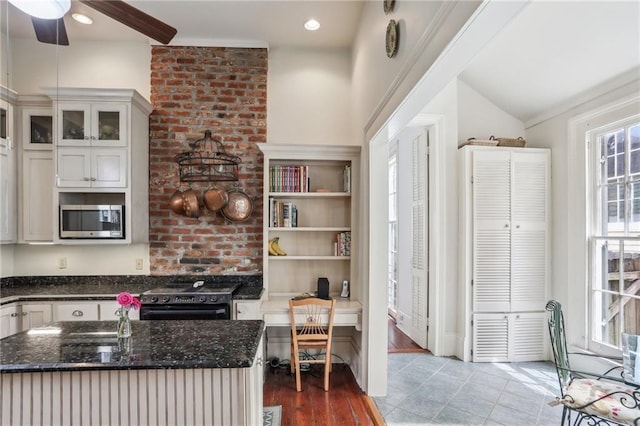 kitchen with a ceiling fan, stainless steel microwave, glass insert cabinets, dark stone counters, and black range with electric cooktop