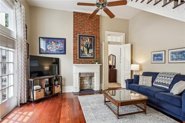 living area with baseboards, ceiling fan, a fireplace, and wood-type flooring