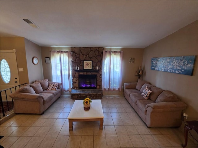 living area featuring plenty of natural light, light tile patterned flooring, a stone fireplace, and visible vents