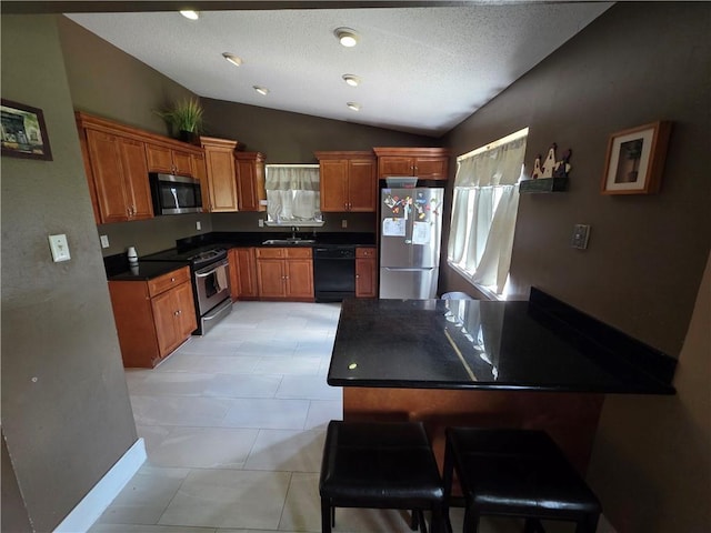 kitchen featuring appliances with stainless steel finishes, dark countertops, vaulted ceiling, brown cabinets, and a sink