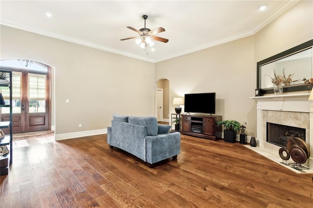 living room featuring crown molding, a fireplace, arched walkways, a ceiling fan, and wood finished floors