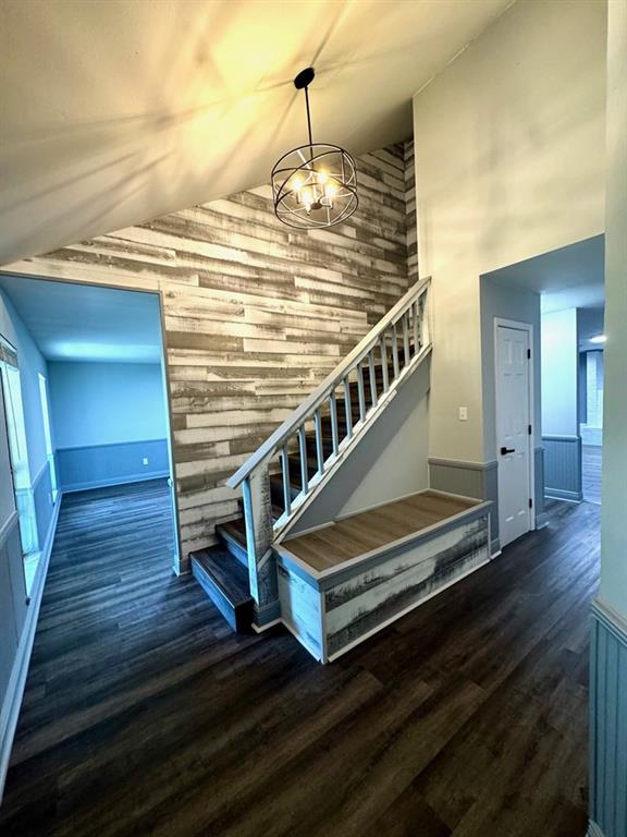 stairs featuring a notable chandelier, high vaulted ceiling, wood walls, and wood finished floors