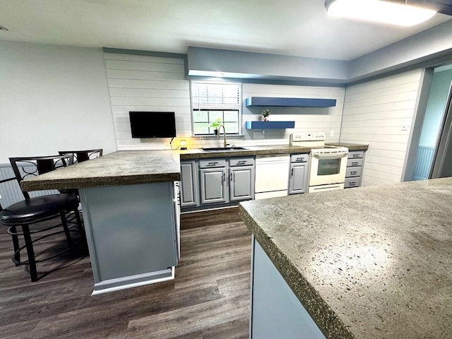 kitchen with a peninsula, dark countertops, white appliances, dark wood-type flooring, and a sink