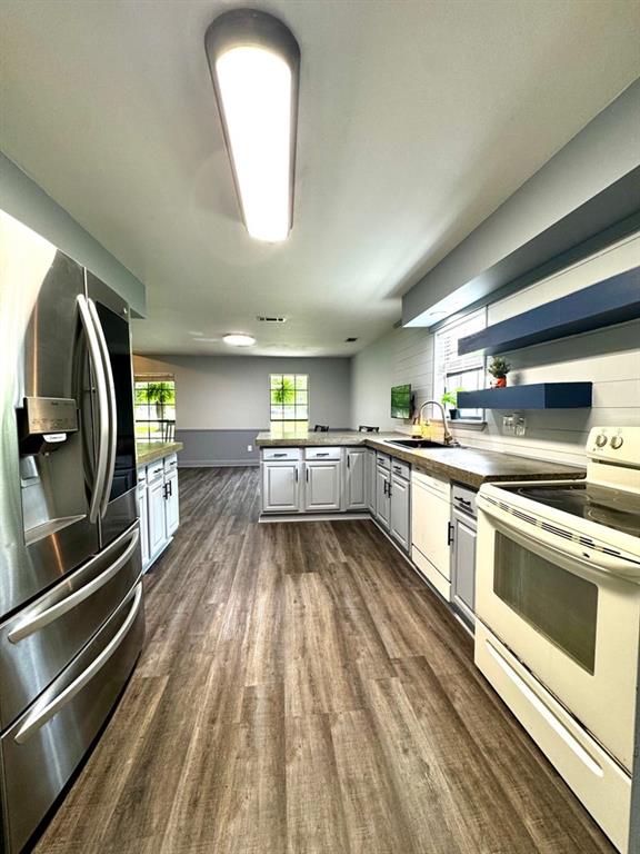 kitchen with a peninsula, white appliances, baseboards, a sink, and dark wood finished floors