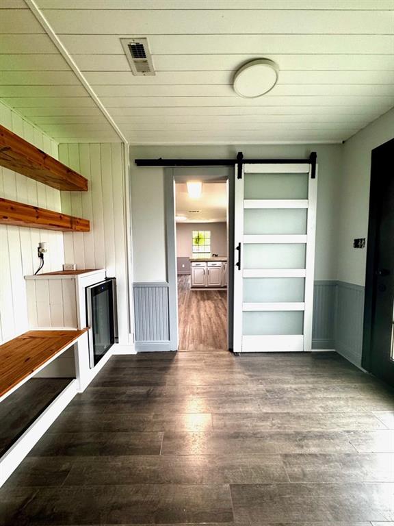 unfurnished living room with wainscoting, a barn door, wooden ceiling, dark wood-type flooring, and visible vents