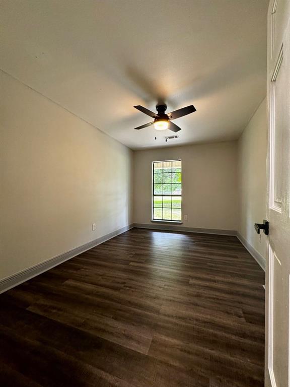 unfurnished room with a ceiling fan, baseboards, visible vents, and dark wood-type flooring