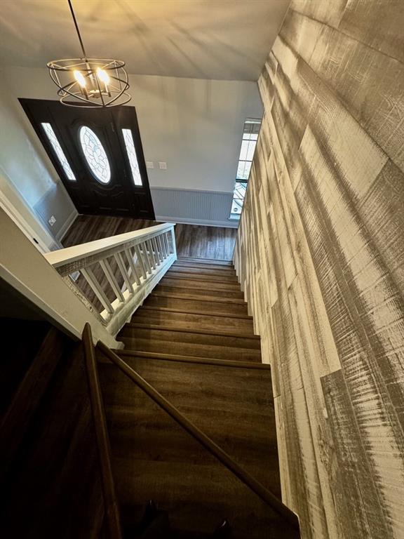 staircase featuring wood finished floors, a chandelier, and a wainscoted wall