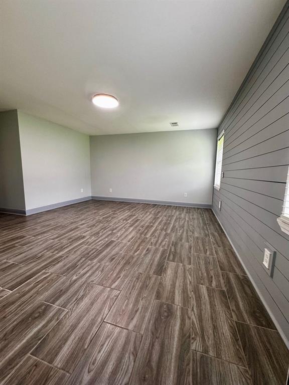 empty room with wooden walls, baseboards, and dark wood-type flooring