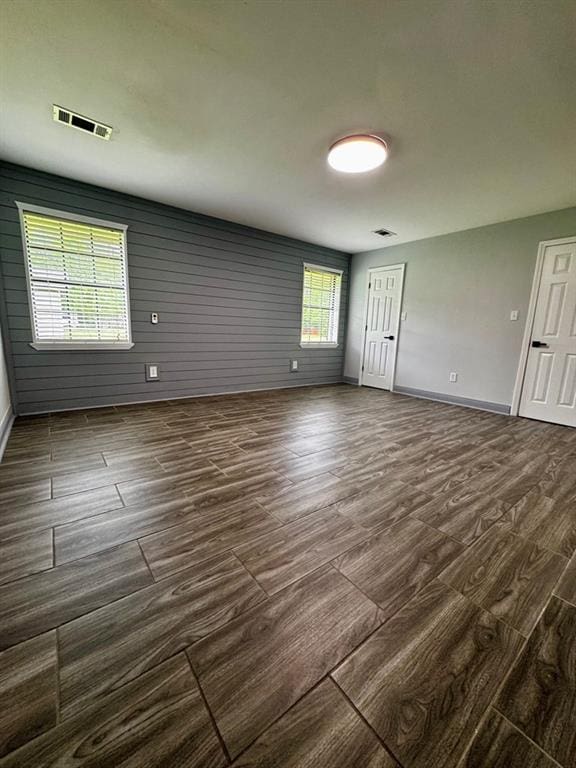 unfurnished room featuring baseboards, dark wood-style floors, and visible vents