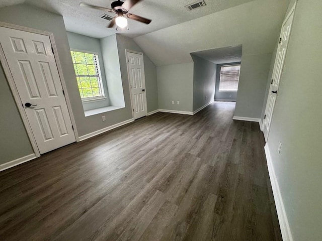 additional living space featuring a textured ceiling, dark wood finished floors, baseboards, vaulted ceiling, and visible vents