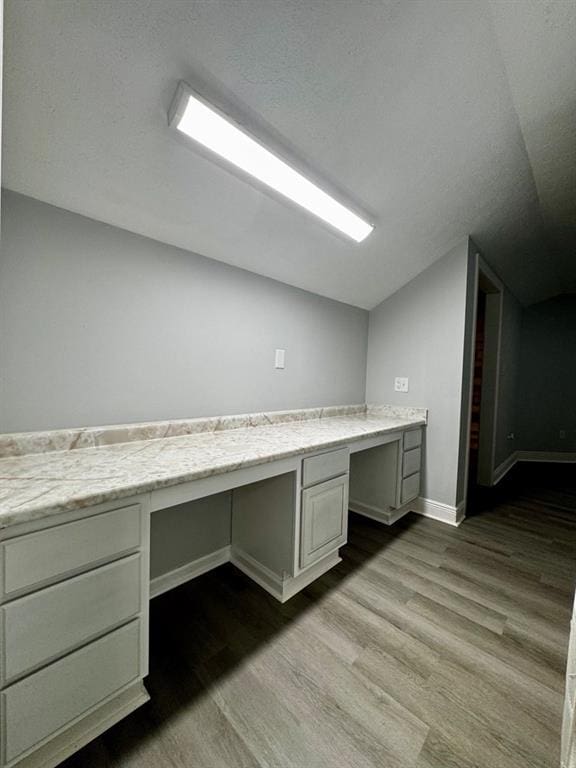 unfurnished office featuring built in study area, baseboards, wood finished floors, and vaulted ceiling