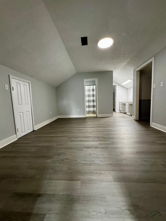 bonus room with baseboards, vaulted ceiling, a textured ceiling, and dark wood-type flooring