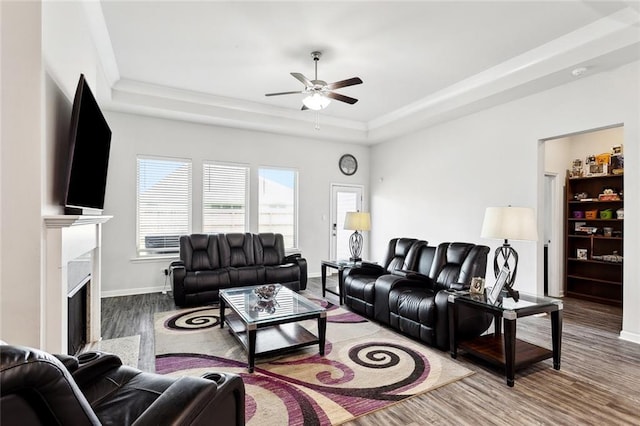 living room with ceiling fan, a raised ceiling, a premium fireplace, baseboards, and wood finished floors