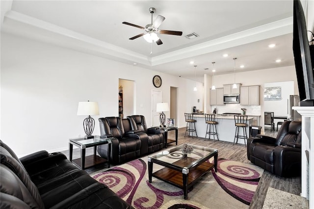 living room with a ceiling fan, visible vents, wood finished floors, a raised ceiling, and recessed lighting