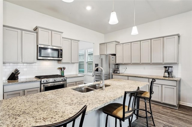 kitchen with gray cabinetry, appliances with stainless steel finishes, a kitchen breakfast bar, and a sink