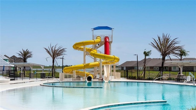 community pool with a water play area, a water slide, and fence