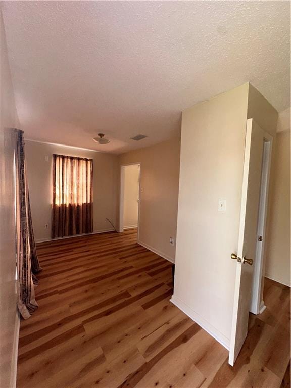 unfurnished room featuring a textured ceiling, baseboards, wood finished floors, and visible vents