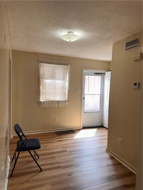 entryway with visible vents, a textured ceiling, baseboards, and light wood-type flooring