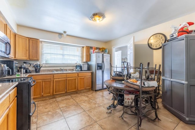 kitchen with brown cabinets, a sink, light tile patterned floors, light countertops, and stainless steel appliances