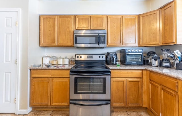 kitchen featuring light tile patterned floors, appliances with stainless steel finishes, brown cabinets, and a toaster