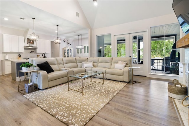 living room with a fireplace with raised hearth, vaulted ceiling, light wood-style flooring, and visible vents