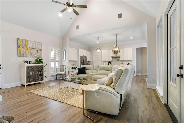 living area with ceiling fan, visible vents, wood finished floors, high vaulted ceiling, and baseboards