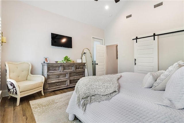 bedroom with high vaulted ceiling, wood finished floors, a barn door, and visible vents