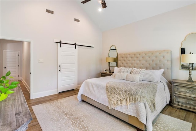 bedroom with high vaulted ceiling, wood finished floors, a barn door, and visible vents