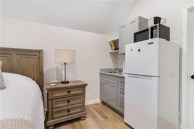 bedroom with freestanding refrigerator, lofted ceiling, a sink, light wood finished floors, and wet bar