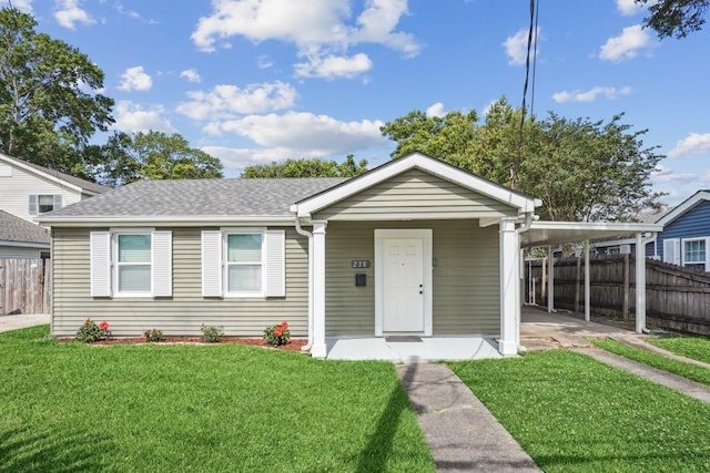 view of front facade with a shingled roof, an attached carport, fence, and a front yard