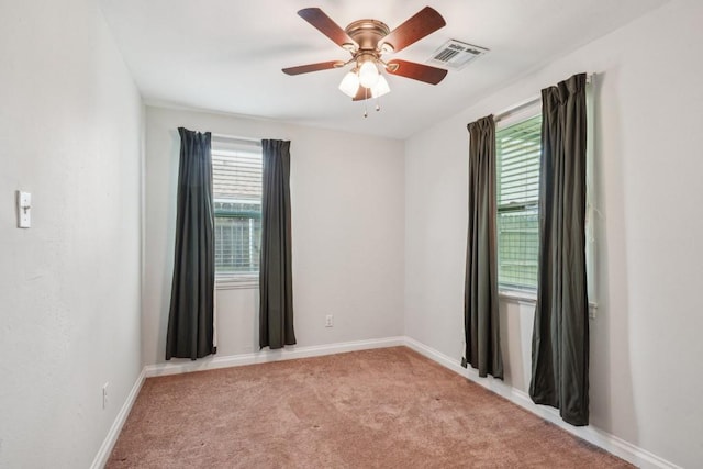 spare room with a ceiling fan, light colored carpet, visible vents, and baseboards