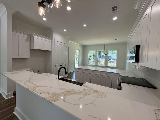 kitchen featuring light stone countertops, a sink, a peninsula, a notable chandelier, and ornamental molding