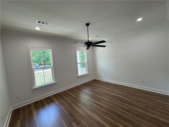 empty room with a ceiling fan, visible vents, dark wood finished floors, baseboards, and ornamental molding