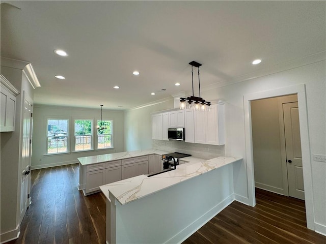 kitchen with a peninsula, stainless steel microwave, light stone countertops, and ornamental molding