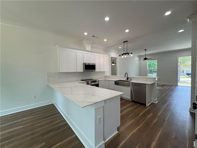 kitchen featuring ornamental molding, a peninsula, baseboards, a sink, and appliances with stainless steel finishes