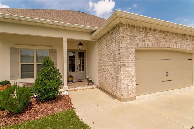 entrance to property featuring a shingled roof, an attached garage, concrete driveway, and brick siding