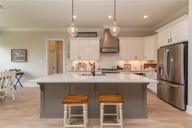 kitchen with a sink, stainless steel fridge with ice dispenser, white cabinets, light countertops, and custom range hood